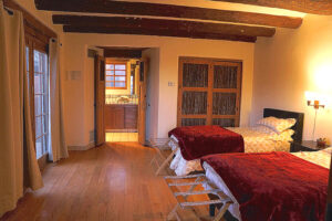 A cozy Southwestern-style bedroom featuring two twin beds with soft white bedding and deep red throws, creating a warm and inviting feel.