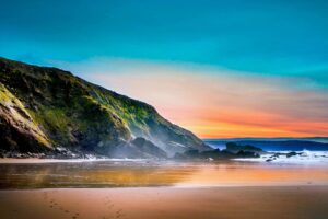 Scenic coastal landscape featuring dramatic cliffs, a sandy beach, and a colorful sunset with shades of orange, pink, and blue. The serene and natural setting evokes tranquility, renewal, and connection with nature, ideal for promoting wellness and retreat experiences.