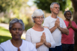 Group meditation in a serene outdoor setting, featuring individuals with eyes closed and hands in prayer position, fostering mindfulness and inner peace.
