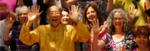 Master Mingtong Gu joyfully celebrating with a diverse group of participants at a Wisdom Healing Qigong event, radiating energy, happiness, and community connection.