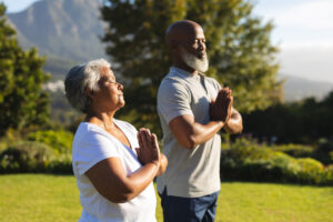 Peaceful outdoor meditation with diverse individuals standing in serene natural surroundings, featuring a backdrop of mountains and trees under a clear sky.