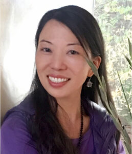 Linling smiling warmly in a serene indoor setting, with natural light and greenery in the background, radiating positivity and calmness.