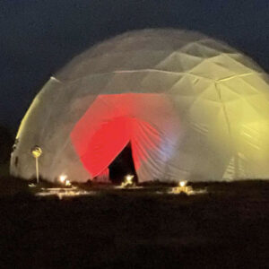 Night view of the Chi Center Dome glowing with vibrant red and yellow lighting, creating a serene and inviting space for healing and meditation in a tranquil setting.