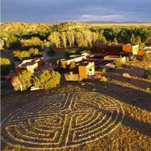 Aerial view of the Chi Center, featuring a beautifully designed labyrinth in the foreground, surrounded by serene natural landscapes and adobe-style buildings under the golden light of sunset.