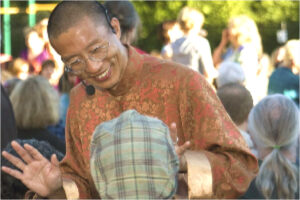 Master Mingtong Gu smiling warmly while interacting with a child during an outdoor gathering, surrounded by a vibrant community atmosphere.