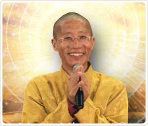 Master Mingtong Gu smiling warmly, wearing a golden robe, holding a microphone with hands in a gesture of gratitude, set against a radiant golden background symbolizing energy and light.