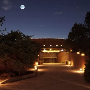 A tranquil nighttime view of the Chi Center entrance, beautifully illuminated by warm lights and set under a starry sky with a glowing full moon.