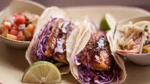 A plate with three tacos and a bowl of coleslaw at The Chi Center