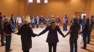 A group of individuals standing in a circle holding hands inside the Chi Center's warm and inviting indoor space.