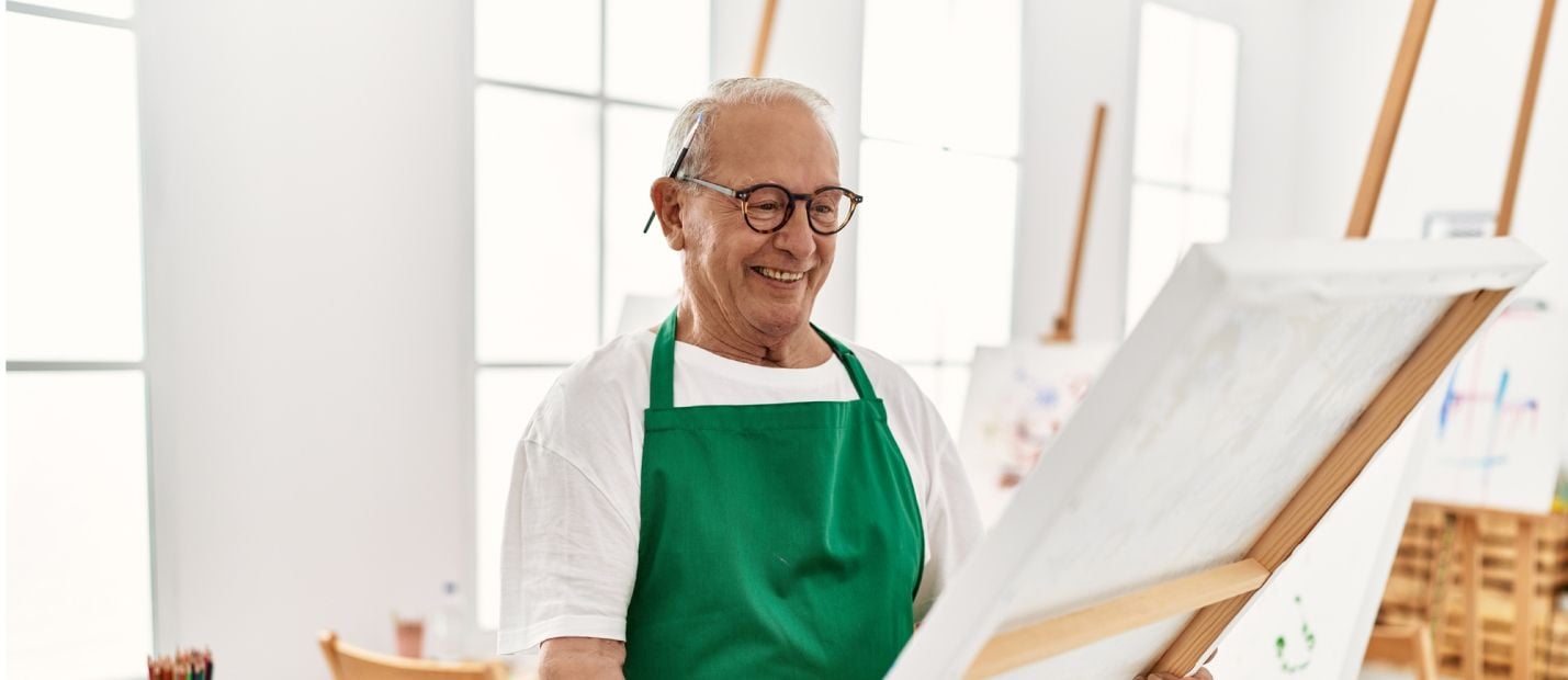 A man in a green apron is painting on an easel.