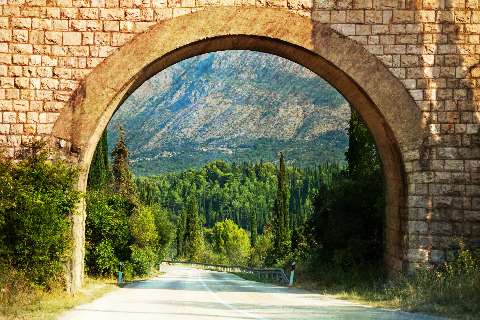A stone arch over a road leading to a mountain.