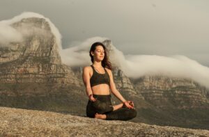 A woman sitting in a Qigong position on top of a mountain.