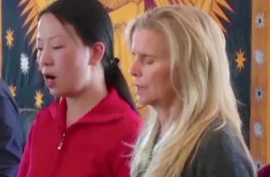 Linling and another participant deeply engaged in a Qigong sound healing session, with a vibrant tapestry featuring celestial designs in the background, creating a serene and focused atmosphere.