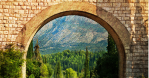 Scenic view through a stone archway framing a lush green landscape and rolling mountains in the distance, highlighting natural beauty and architectural charm.