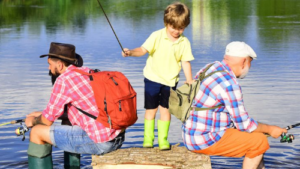 Three generations fishing together by the lake: a grandfather, father, and young boy enjoying quality time outdoors.