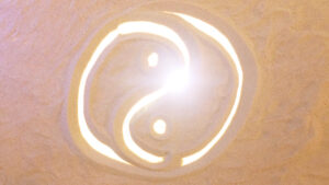 Illuminated yin-yang symbol drawn in sand with radiant light shining from the center, symbolizing balance and harmony.