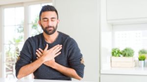 Man practicing mindfulness and gratitude with hands over his heart, sitting peacefully in a bright, serene kitchen environment.
