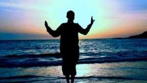 Silhouette of a person practicing Qigong by the ocean at sunset, with arms raised in harmony, reflecting peace and connection with nature.