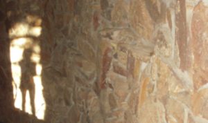 Stone wall with sunlight casting a silhouette of a person, creating a serene and mysterious visual effect in a natural setting.