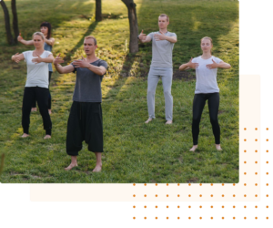 Group practicing Qigong outdoors on a grassy field, focusing on mindful movements and energy flow under the shade of trees, promoting health and relaxation.