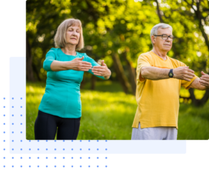 Older man and woman practicing Qigong exercises outdoors in a lush green park, focusing on gentle movements and mindfulness under the warm sunlight.