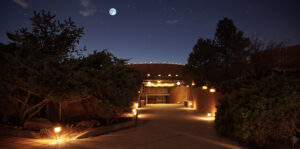 Evening view of the Kiva at the Southwest Sanctuary, illuminated by warm lights under a starry sky and glowing full moon.