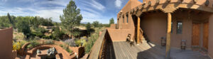 Close-up view of The Chi Center's adobe architecture, featuring traditional vigas against a backdrop of blue skies and wispy clouds, capturing the essence of Southwest design in Galisteo, New Mexico.