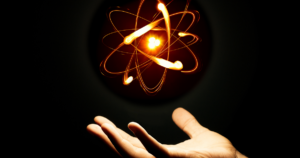 Hand reaching upward with a glowing atomic structure floating above, symbolizing energy, science, and the power of creation in a dark, dramatic background.