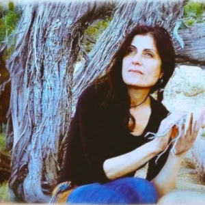 Portrait of Martha Reich sitting outdoors near a weathered tree, gazing thoughtfully into the distance, surrounded by natural beauty and tranquility.