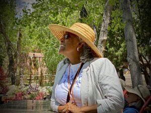 Joyful woman in a straw hat enjoying a sunny day in a lush garden setting, surrounded by greenery and vibrant energy.
