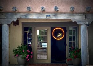 Entrance to The Chi Center, featuring traditional Southwestern architecture, a glowing circular logo, and vibrant potted flowers on either side of the doorway.