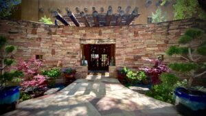 Reception entrance at The Chi Center, featuring a rustic stone wall, decorative wooden beams, vibrant greenery, and colorful potted plants, framed by peaceful Buddha statues.