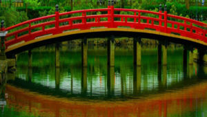 Vibrant red arched bridge spanning a tranquil pond, surrounded by lush green vegetation, symbolizing harmony and connection.