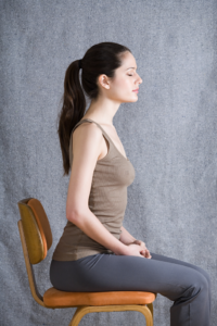 Side profile of a serene woman with a ponytail meditating against a neutral gray textured background, eyes closed in peaceful contemplation.