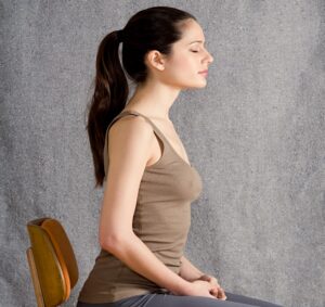 Side profile of a serene woman with a ponytail meditating against a neutral gray textured background, eyes closed in peaceful contemplation.