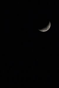 A crescent moon glowing softly against a dark, starless night sky, showcasing its craters and surface details in a serene celestial view.