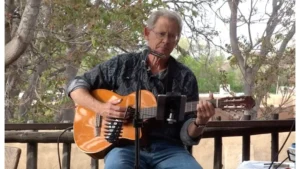 Chris Harrell performing music outdoors with a guitar and microphone, surrounded by trees and a peaceful natural setting.