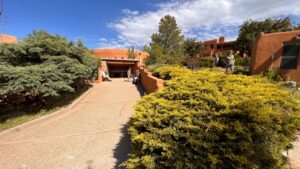 The Chi Center entrance featuring adobe-style architecture, lush greenery, and visitors enjoying the serene outdoor environment under a bright blue sky.