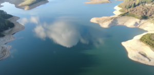 A breathtaking aerial view of a serene lake surrounded by lush green hills and forests, showcasing the tranquility and natural beauty of the landscape.