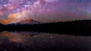 Majestic mountain under a vibrant night sky filled with stars and the Milky Way, reflected beautifully in a calm lake, creating a serene and mystical landscape.