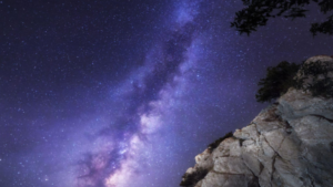 Stunning Milky Way galaxy illuminating the night sky above rugged cliffs, framed by tree branches, showcasing the beauty of nature and the cosmos.