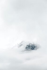 Snow-capped mountain peak partially veiled by soft clouds, creating a serene and minimalist winter landscape.