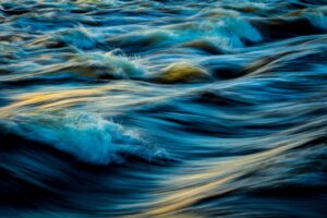 Flowing water with soft ripples and golden light reflections, symbolizing movement, serenity, and natural harmony.