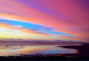 Vivid sunset over a serene beach with colorful pink, orange, and blue hues reflecting on the calm ocean water, creating a peaceful and inspiring scene.