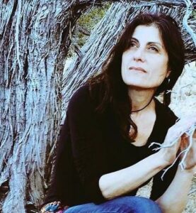 Portrait of Martha Reich sitting thoughtfully by an ancient tree, with natural light highlighting her serene expression and connection to nature