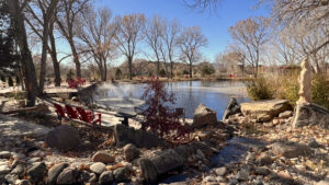Peaceful garden scene featuring a pond with a water fountain, red chairs, a statue of the Goddess of Compassion, and natural landscaping with trees and rocks, creating a serene retreat atmosphere.