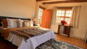 Cozy and sunlit bedroom in Pueblo House #1 - APACHE, featuring Southwestern-style decor, wooden beams, a comfortable bed with patterned blankets, and a warm, rustic ambiance.