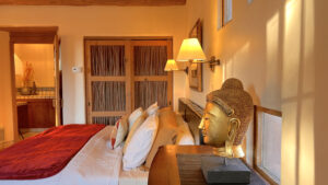 Tranquil bedroom featuring a golden Buddha statue, rustic Southwestern design elements, warm lighting, and a cozy bed with red accents, creating a serene and meditative atmosphere.