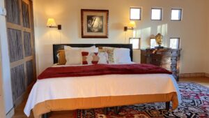 Elegant Southwestern bedroom with a large bed, red and white bedding, decorative pillows, wooden accents, and a golden Buddha statue on a dresser, creating a warm and peaceful retreat atmosphere.