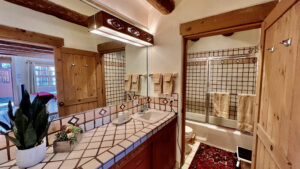 Beautifully designed Pueblo-style bathroom featuring traditional tile work, rustic wooden beams, elegant lighting, and a cozy shower area with sliding glass doors at The Chi Center.
